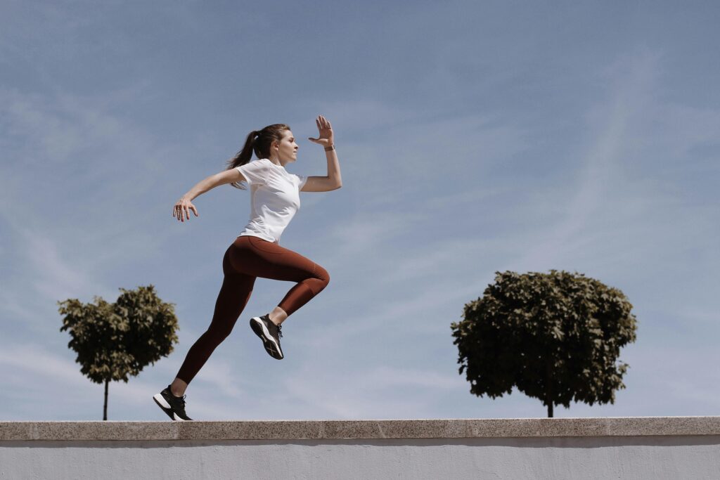 Athletic woman running on an outdoor road, demonstrating fitness and determination under a blue sky.