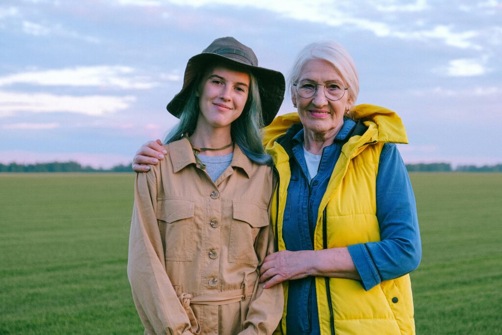 Senior woman and younger woman smiling together outdoors in a green field.