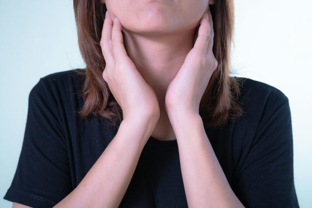 Close-up of a woman touching her neck, possibly indicating discomfort or throat pain.